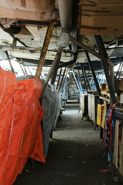 The image shows the interior of a packing and loading area within a bus or van used for home relocation, with a view down a narrow aisle. On the left side, large objects are wrapped in orange and grey